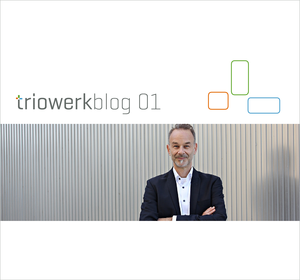 Der Triowerk-Gründer, Christian Olbrich, steht im Anzug mit weißem Hemd vor einer gerippten Aluminiumwand. Darüber steht Triowerk-Blog, daneben ist das Triowerk-Logo zu sehen.